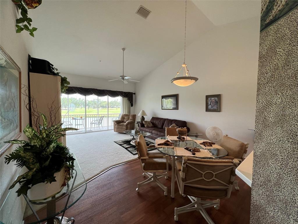 A living and dining area with vaulted ceilings, carpeted and wood flooring, and a balcony view — 6632 PINEVIEW TERRACE UNIT 10-201, BRADENTON, FL