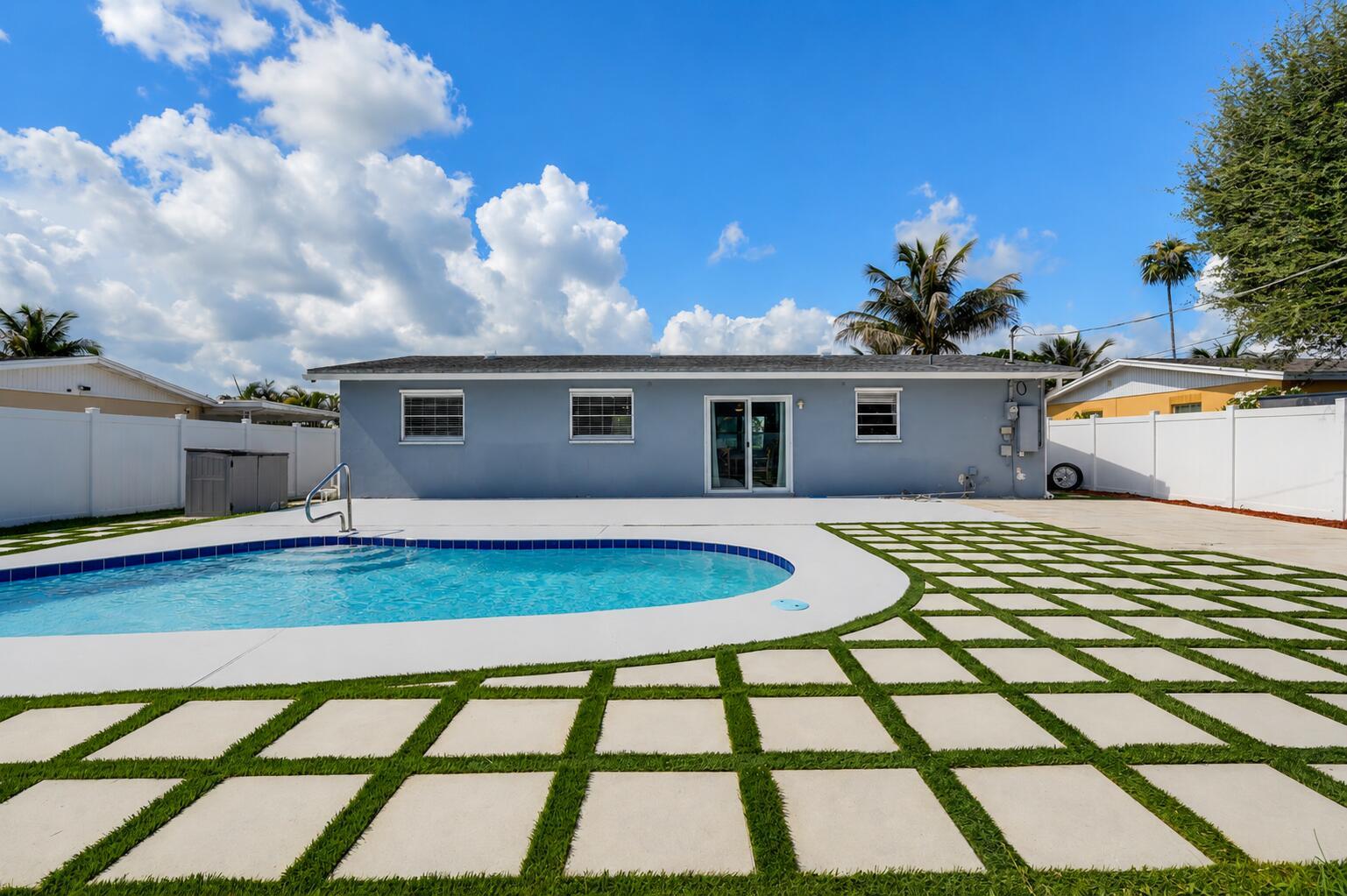 A backyard features a swimming pool, a gray house, and a grid of concrete pavers — 6091 Fair Green Road, West Palm Beach FL 33417, WEST PALM BEACH, FL