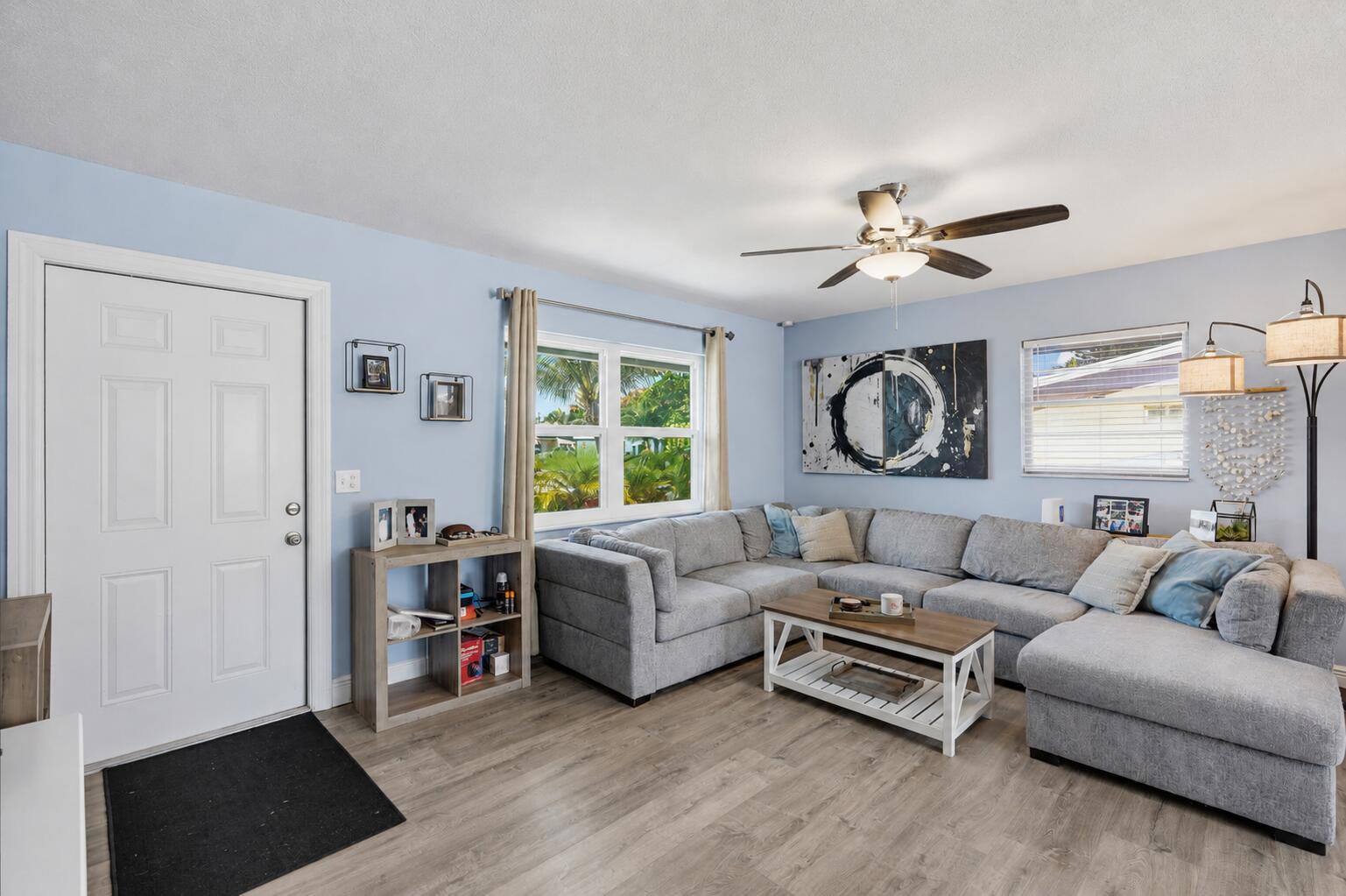 A living room features light blue walls, a gray sectional sofa, and wood-look flooring — 6091 Fair Green Road, West Palm Beach FL 33417, WEST PALM BEACH, FL