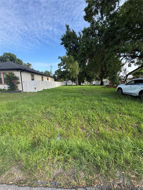 A grassy vacant lot sits next to a white house with a white fence — 2710 W LAKE AVENUE, TAMPA, FL