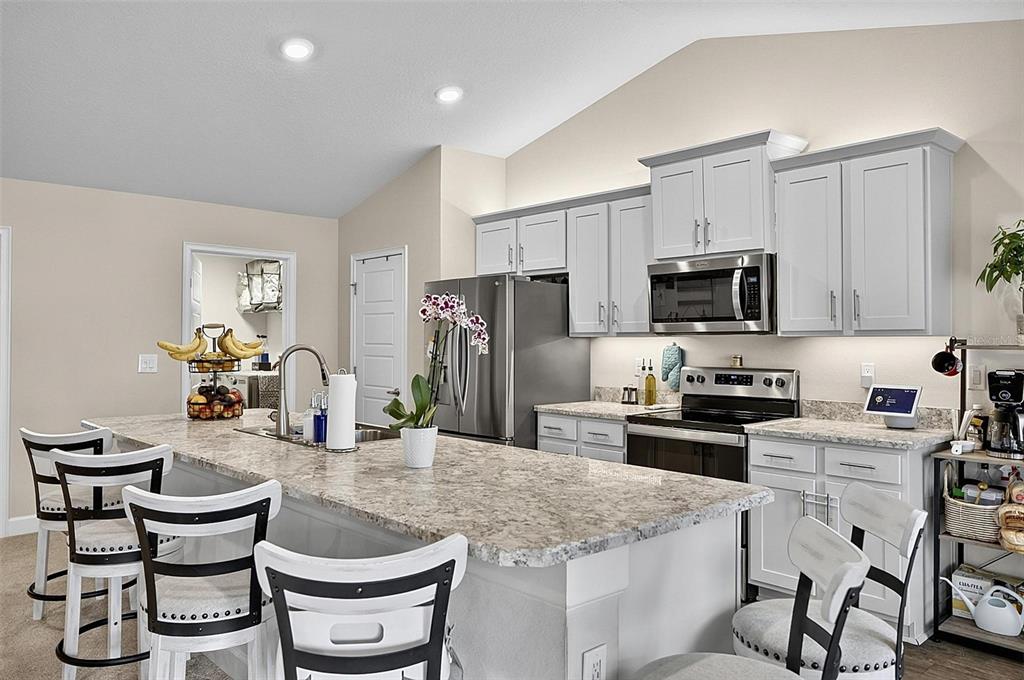 A kitchen with light gray cabinets, granite countertops, a center island, and white bar stools — 33 RICHARDSON DRIVE, PALM COAST, FL