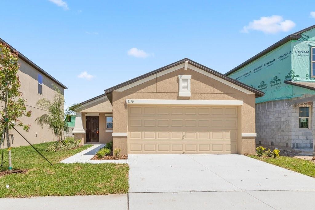 A tan, single-story house with a two-car garage and a partially constructed neighboring home — 7110 AMELIA COVE COURT, SUN CITY CENTER, FL