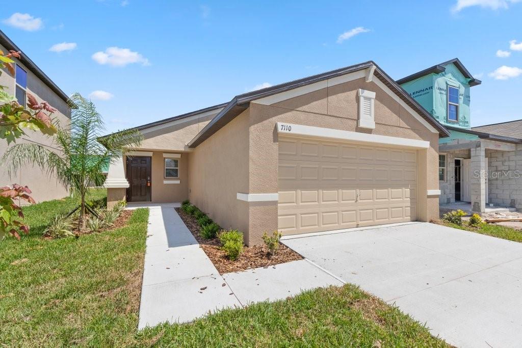 A tan, single-story suburban house with a two-car garage and a concrete walkway — 7110 AMELIA COVE COURT, SUN CITY CENTER, FL
