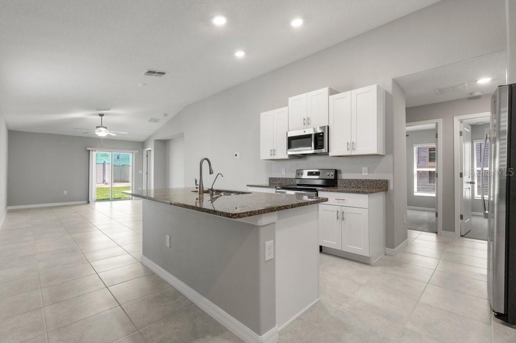 A kitchen with white cabinets, granite countertops, and an island opens to a living area — 7110 AMELIA COVE COURT, SUN CITY CENTER, FL