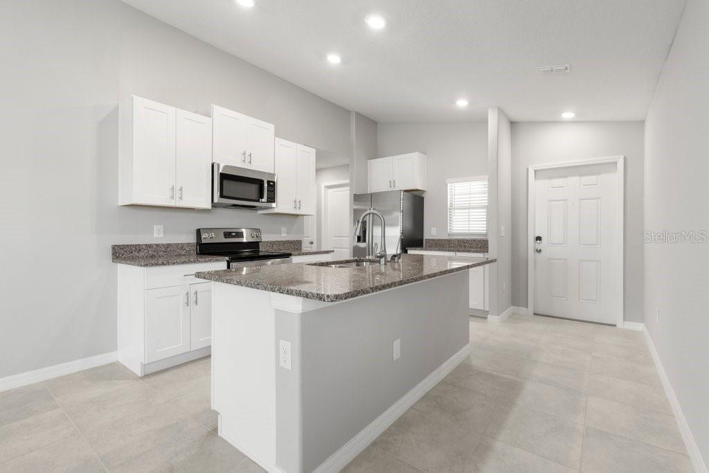 A modern kitchen features white cabinets, granite countertops, a central island, and stainless steel appliances — 7110 AMELIA COVE COURT, SUN CITY CENTER, FL