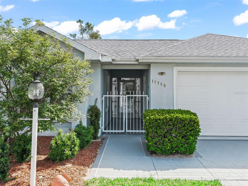 The exterior of a single-story house features a gated entryway and a white garage door — 17789 SE 113TH TERRACE, SUMMERFIELD, FL