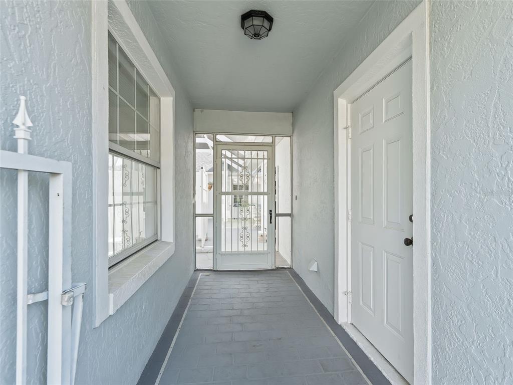 A covered entryway features a white door, a screened door, and gray tiled flooring — 17789 SE 113TH TERRACE, SUMMERFIELD, FL