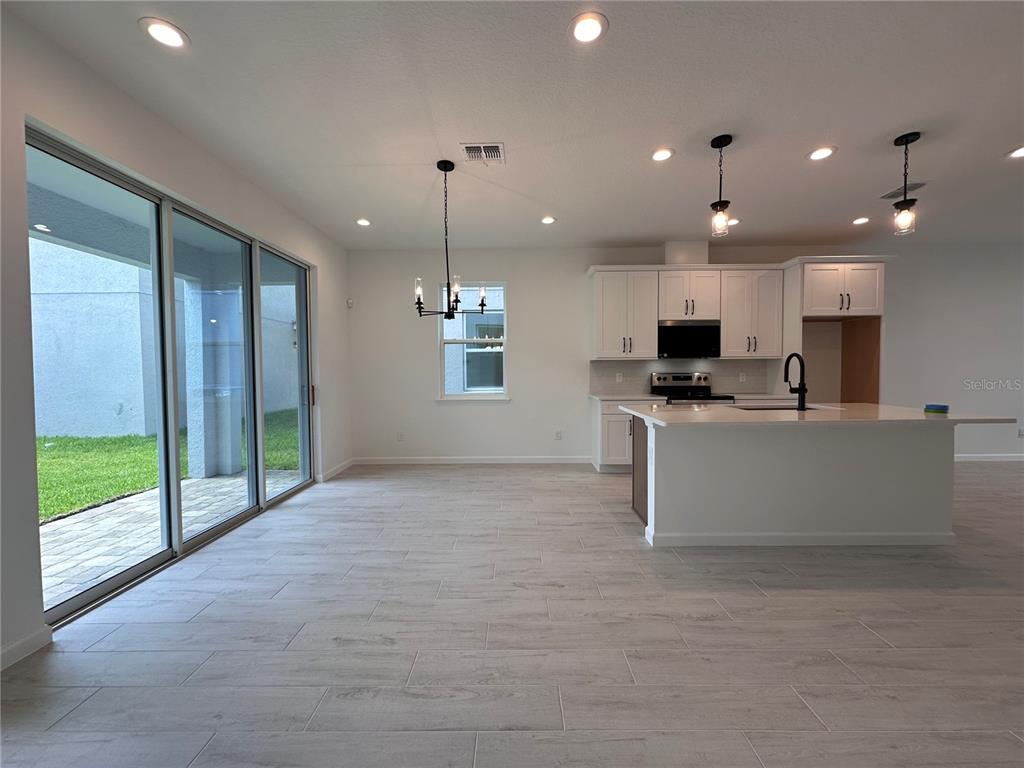 A modern kitchen and dining area feature white cabinetry, a center island, and sliding glass doors — 12899 WESTHAVEN OAK DRIVE, WINTER GARDEN, FL