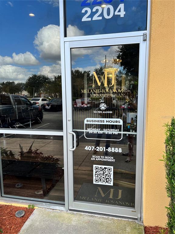 The exterior of a commercial storefront features a glass door with business hours and branding — 2204 W COLUMBIA AVENUE, KISSIMMEE, FL