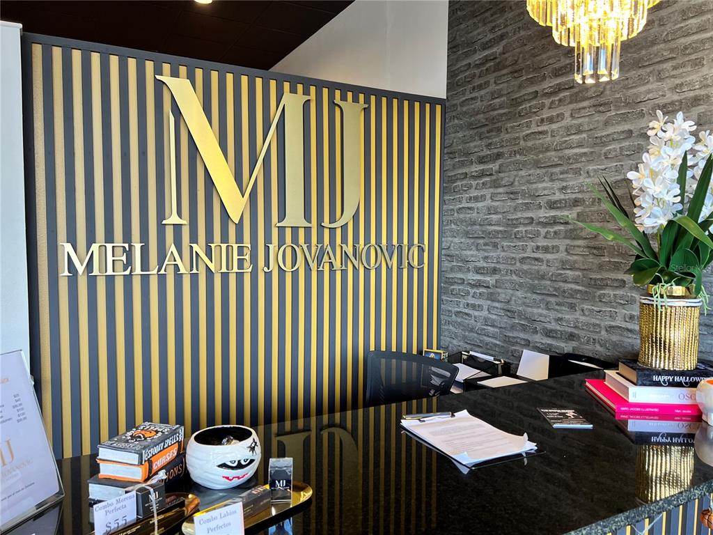 A reception desk features a gold and black striped wall with a Melanie Jovanovic logo — 2204 W COLUMBIA AVENUE, KISSIMMEE, FL