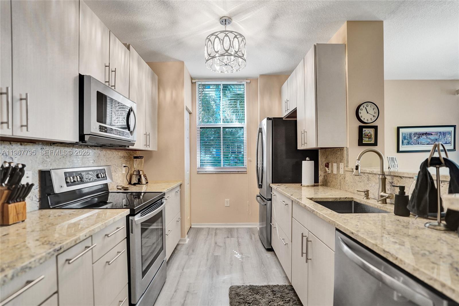 A galley kitchen features light-colored cabinetry, granite countertops, stainless steel appliances, and a window — 2421 NE 65th St # 202, Fort Lauderdale FL 33308, FORT LAUDERDALE, FL