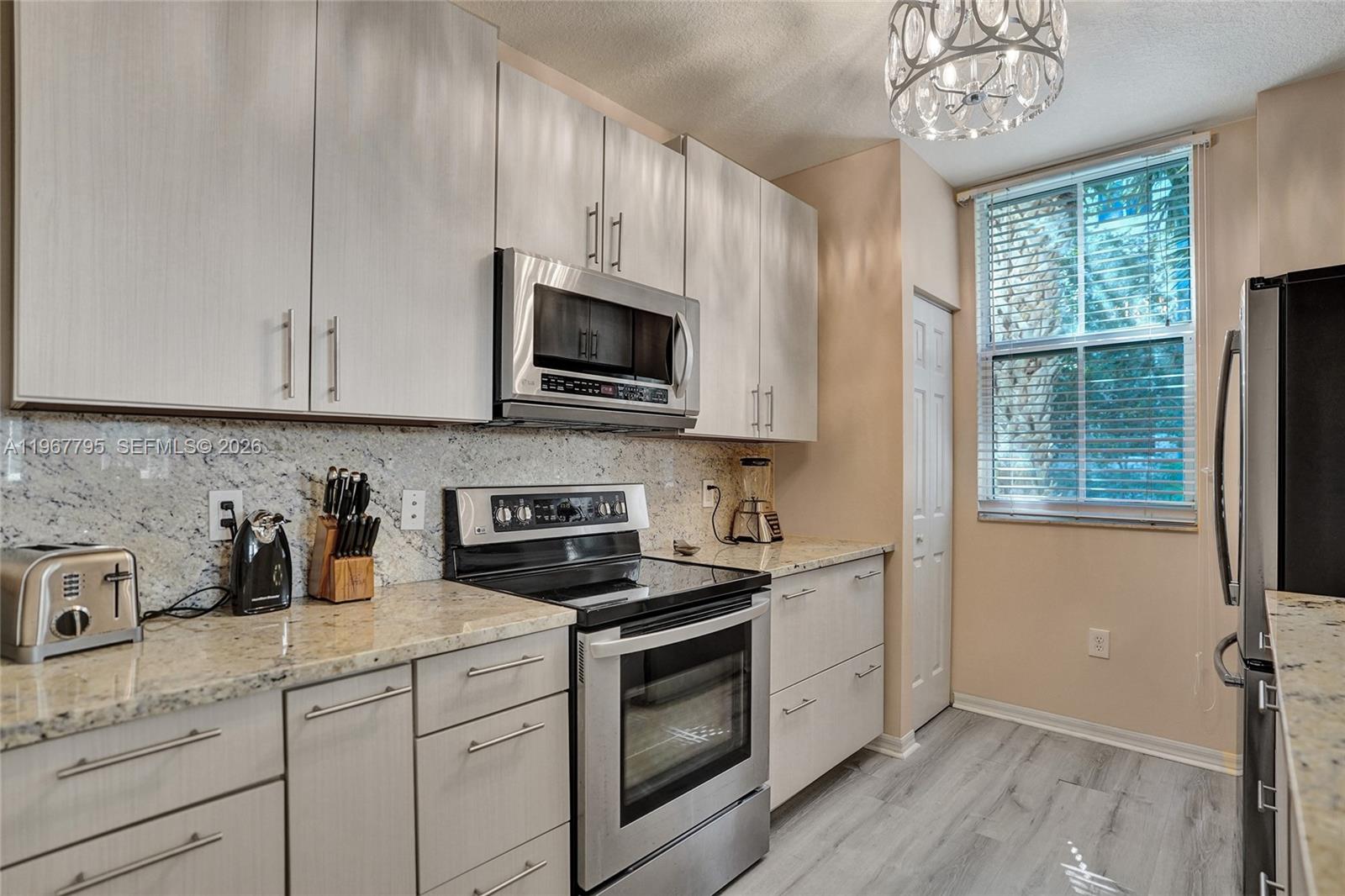 A kitchen features light wood cabinets, stainless steel appliances, granite countertops, and a window — 2421 NE 65th St # 202, Fort Lauderdale FL 33308, FORT LAUDERDALE, FL