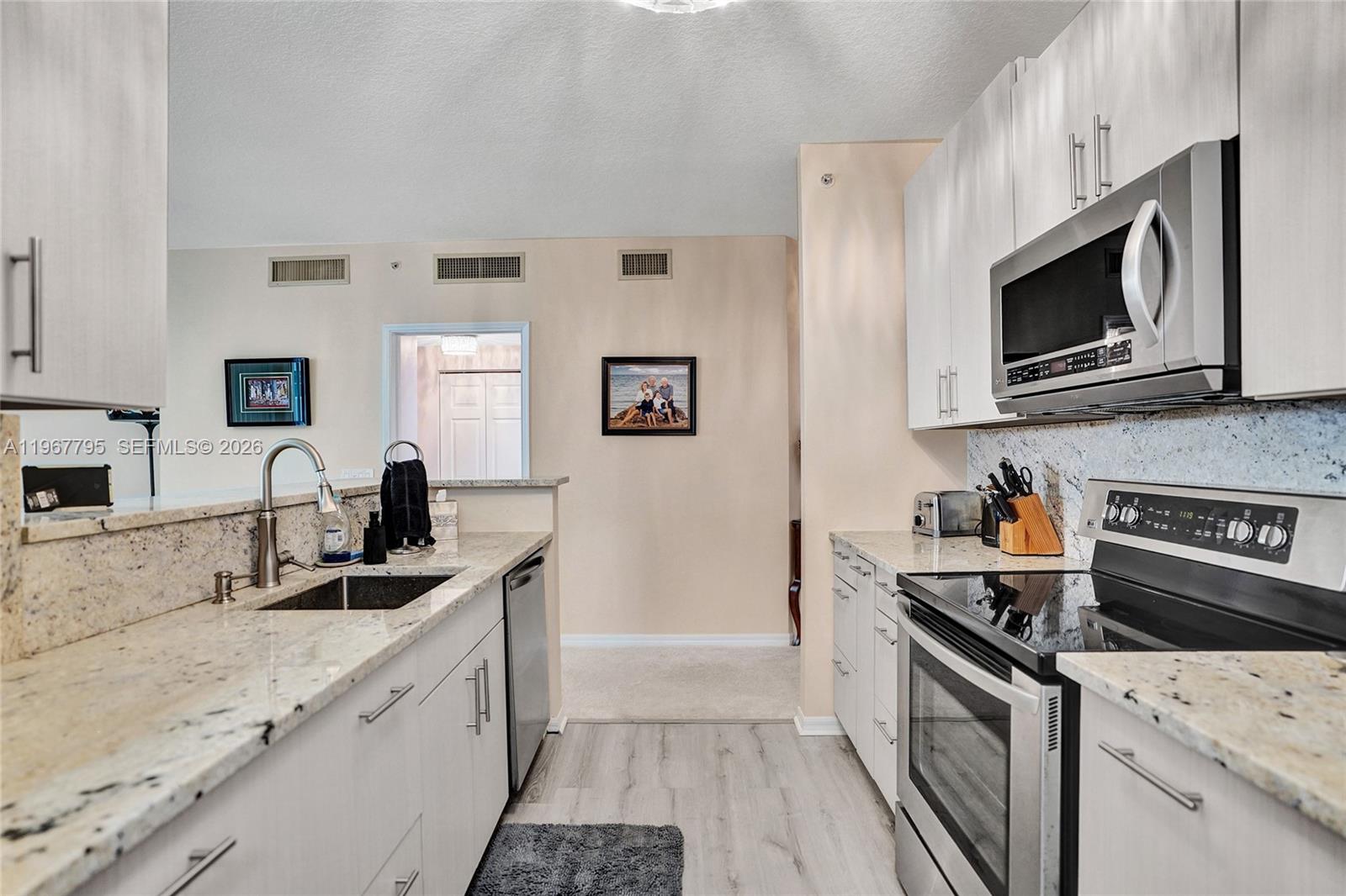 A kitchen features white cabinets, granite countertops, and stainless steel appliances — 2421 NE 65th St # 202, Fort Lauderdale FL 33308, FORT LAUDERDALE, FL