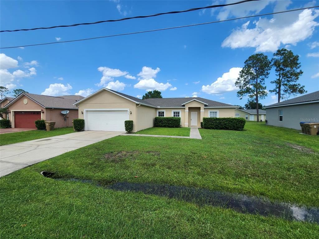 A single-story house with a two-car garage, tan stucco exterior, and a green lawn — 929 GLOUCESTER COURT, KISSIMMEE, FL