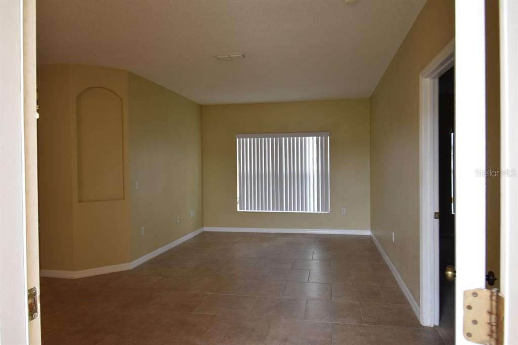 An empty room features tan walls, tile flooring, and a window with vertical blinds — 929 GLOUCESTER COURT, KISSIMMEE, FL