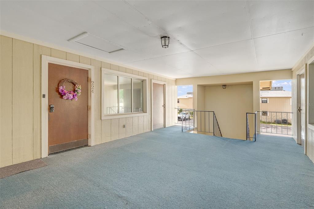 A covered outdoor walkway features blue carpeting, a brown door, and a metal staircase — 4304 LONDON TOWN ROAD UNIT D224, TITUSVILLE, FL