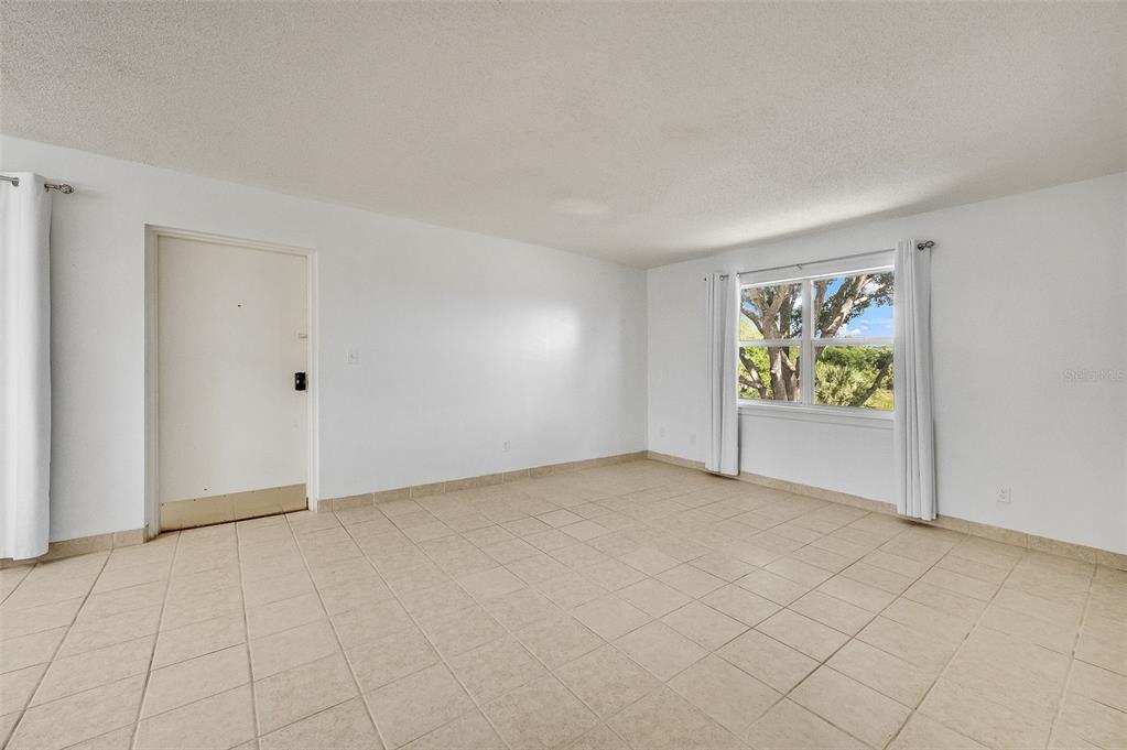 An empty room with white walls, tiled flooring, a white door, and a window — 4304 LONDON TOWN ROAD UNIT D224, TITUSVILLE, FL