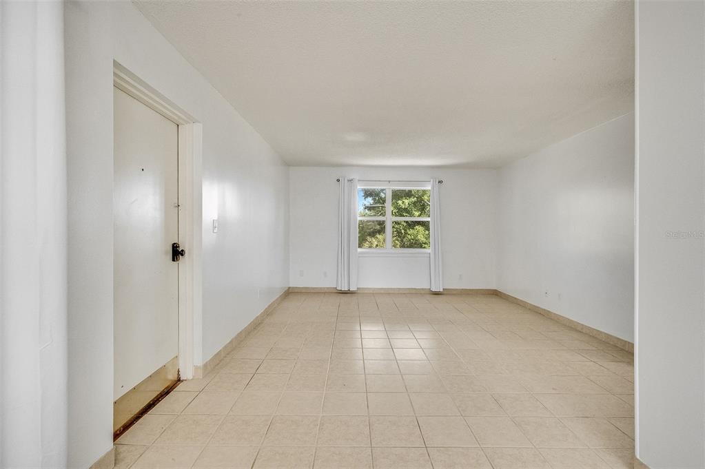 An empty room with white walls, tile flooring, and a single window with curtains — 4304 LONDON TOWN ROAD UNIT D224, TITUSVILLE, FL
