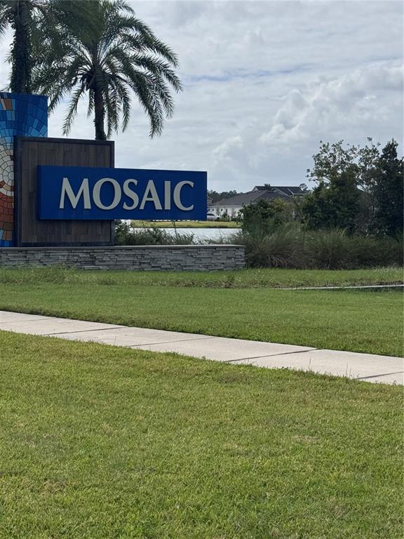 A blue sign with the word Mosaic stands in a grassy area near a pond — 525 MOSAIC BOULEVARD, DAYTONA BEACH, FL