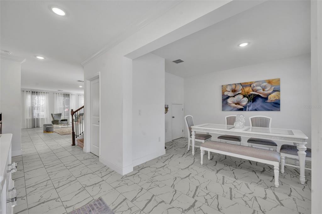 A dining area with white furniture and marble-patterned tile flooring leads to a living space — 1045 BRADFORD RIDGE DRIVE, LEESBURG, FL