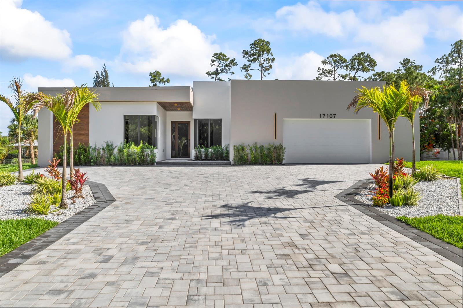 A modern single-story house with a paved driveway, palm trees, and a two-car garage — 17107 W Sycamore Drive W, FL 33470, FL