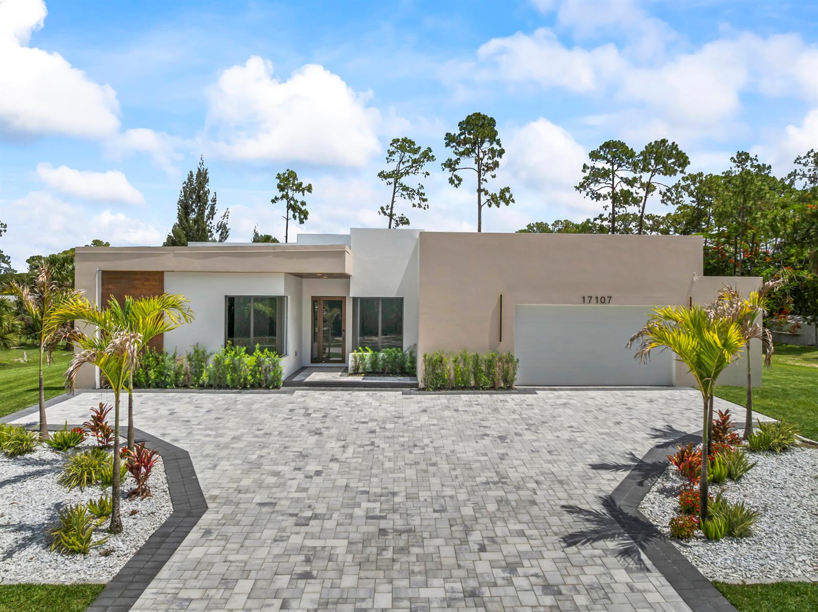 A modern single-story house with a paved driveway, palm trees, and a two-car garage — 17107 W Sycamore Drive W, FL 33470, FL