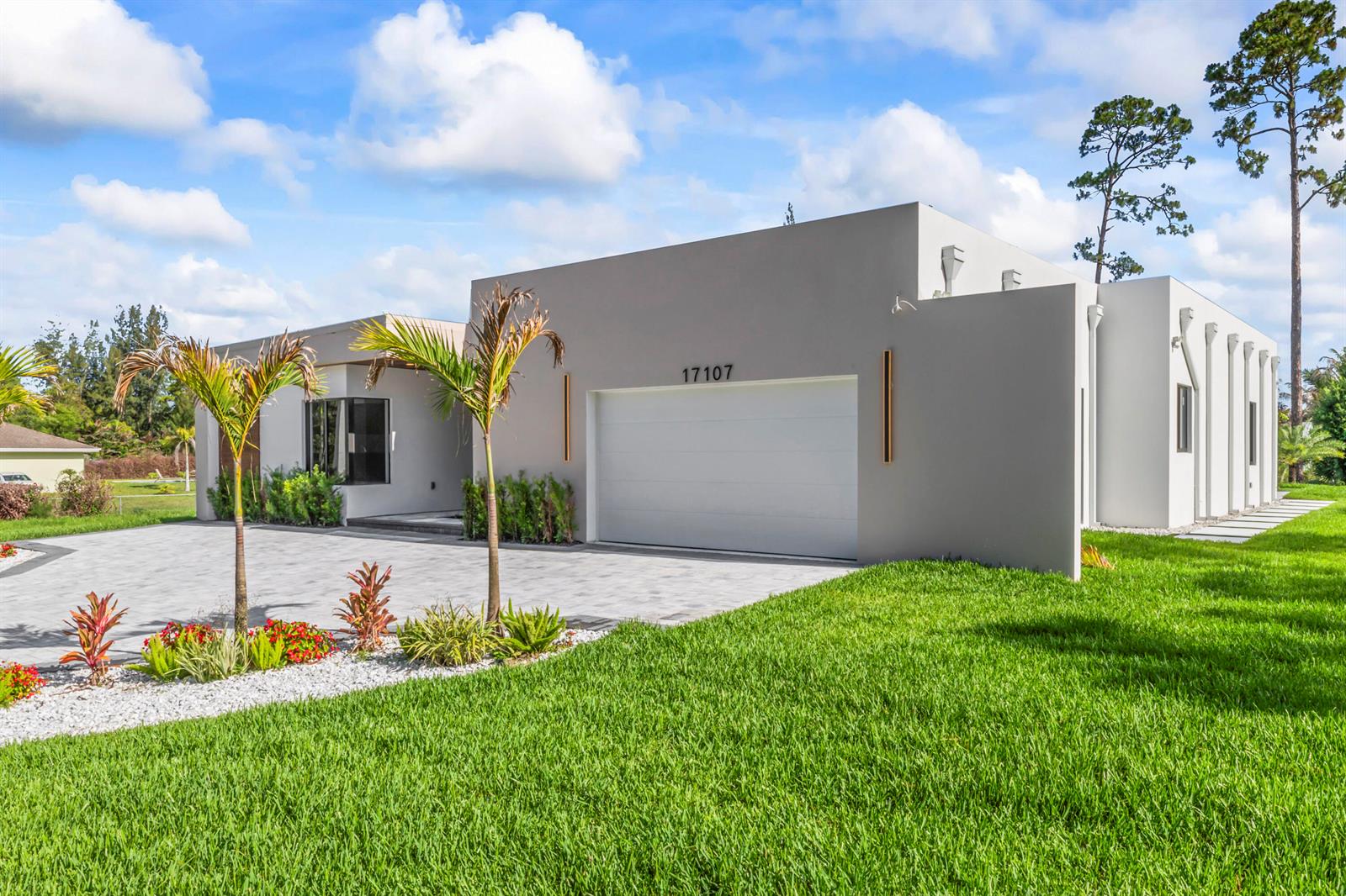 A modern, flat-roofed house with a gray facade, a two-car garage, and palm trees — 17107 W Sycamore Drive W, FL 33470, FL