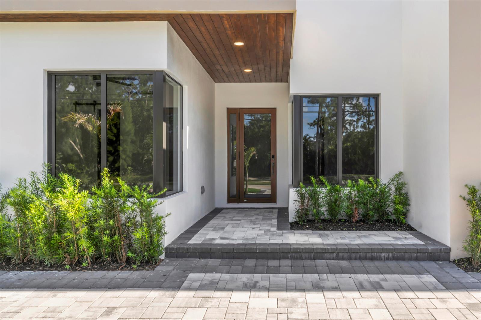 The exterior of a modern home features a wood-paneled entryway, glass door, and paver walkway — 17107 W Sycamore Drive W, FL 33470, FL
