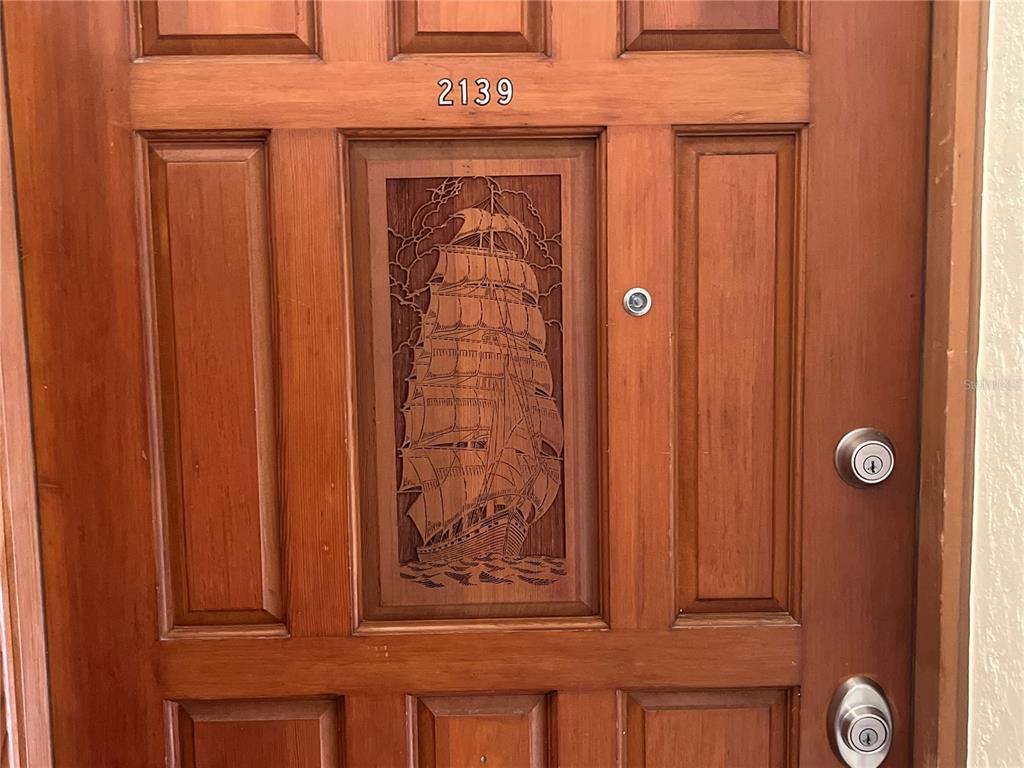 A wooden front door features a carved sailing ship panel and two metal locks — 2139 N OCEAN SHORE BOULEVARD UNIT 2139, FLAGLER BEACH, FL