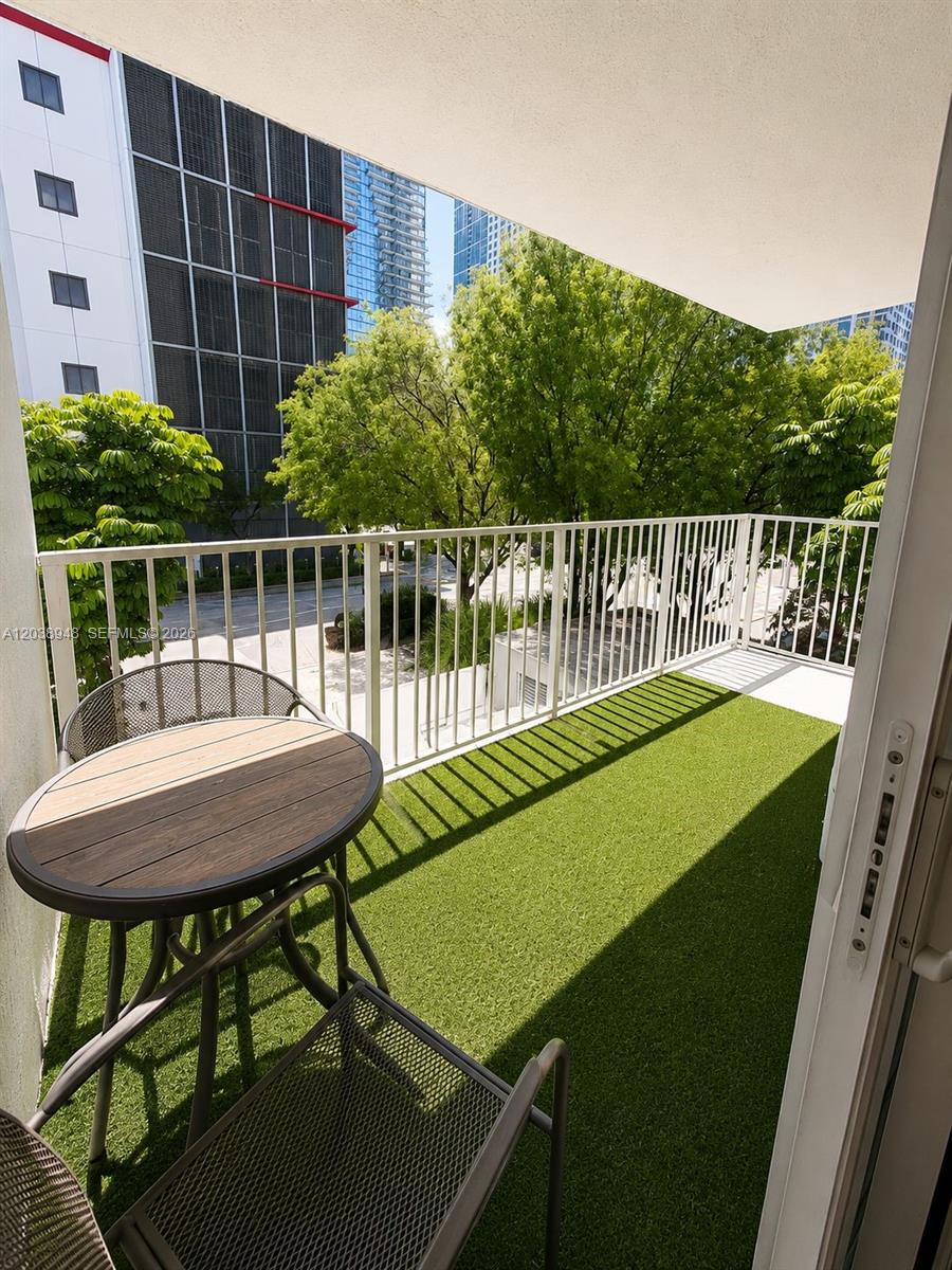 A balcony with artificial turf, a small round table, and two chairs overlooks city trees — 800 N Miami Ave # 305, Miami FL 33136, MIAMI, FL