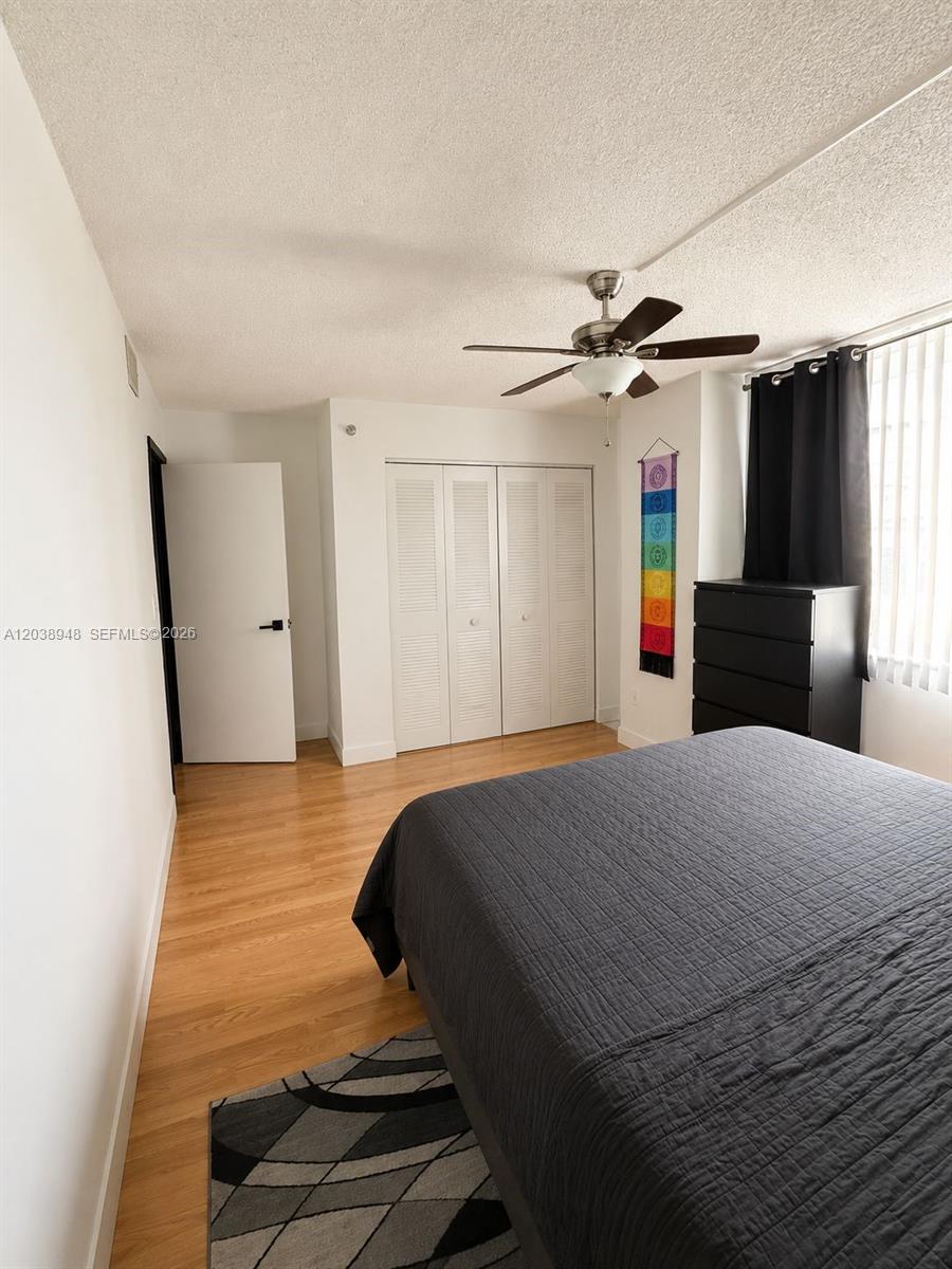 A bedroom features wood flooring, a ceiling fan, a bed, and white louvered closet doors — 800 N Miami Ave # 305, Miami FL 33136, MIAMI, FL