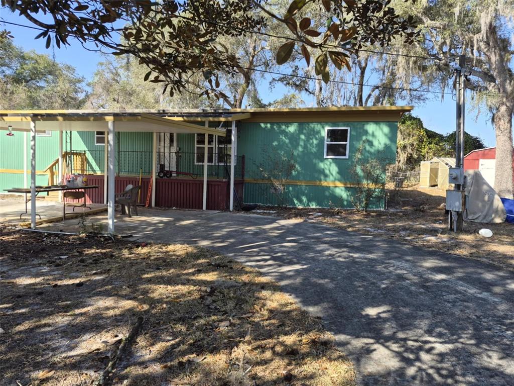 A green mobile home with a metal carport and a paved driveway under large trees — 18565 SE 24TH LANE, OCKLAWAHA, FL