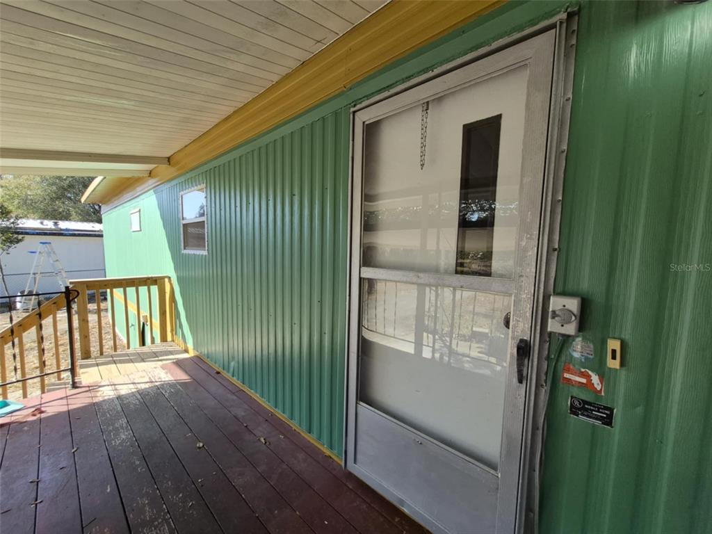 A wooden deck leads to a green metal-sided mobile home with a screen door — 18565 SE 24TH LANE, OCKLAWAHA, FL