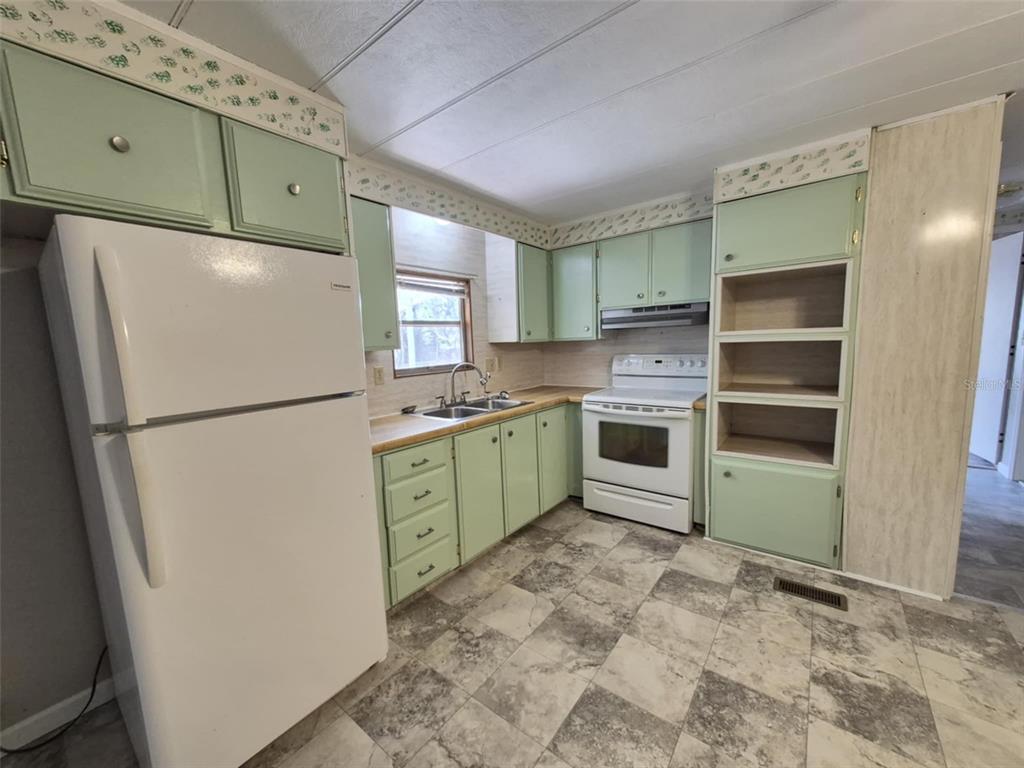 A kitchen features light green cabinets, white appliances, a wood-look countertop, and patterned vinyl flooring — 18565 SE 24TH LANE, OCKLAWAHA, FL