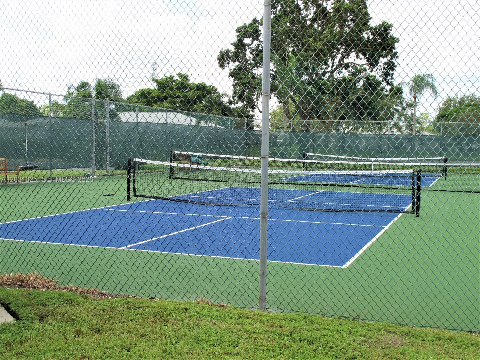 A fenced-in outdoor pickleball court with blue playing surfaces and green surrounding areas — 14529 Canalview Dr # B, Delray Beach FL 33484, DELRAY BEACH, FL