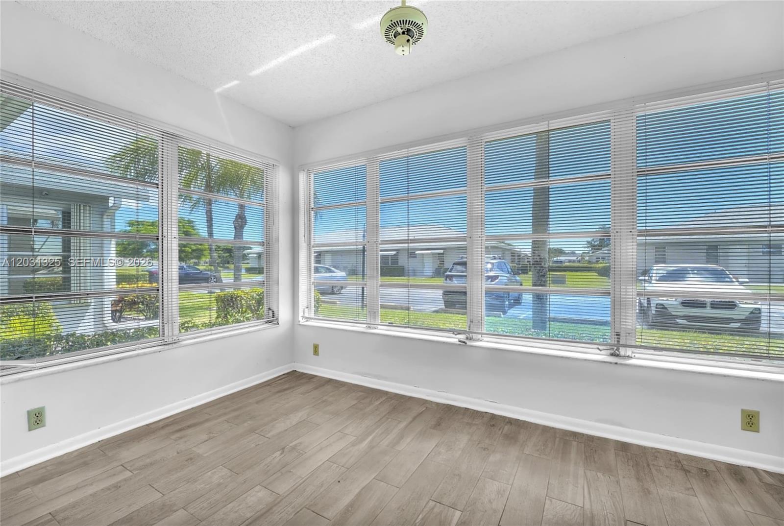 A sunroom features light wood-look flooring, white walls, and large windows with horizontal blinds — 14529 Canalview Dr # B, Delray Beach FL 33484, DELRAY BEACH, FL