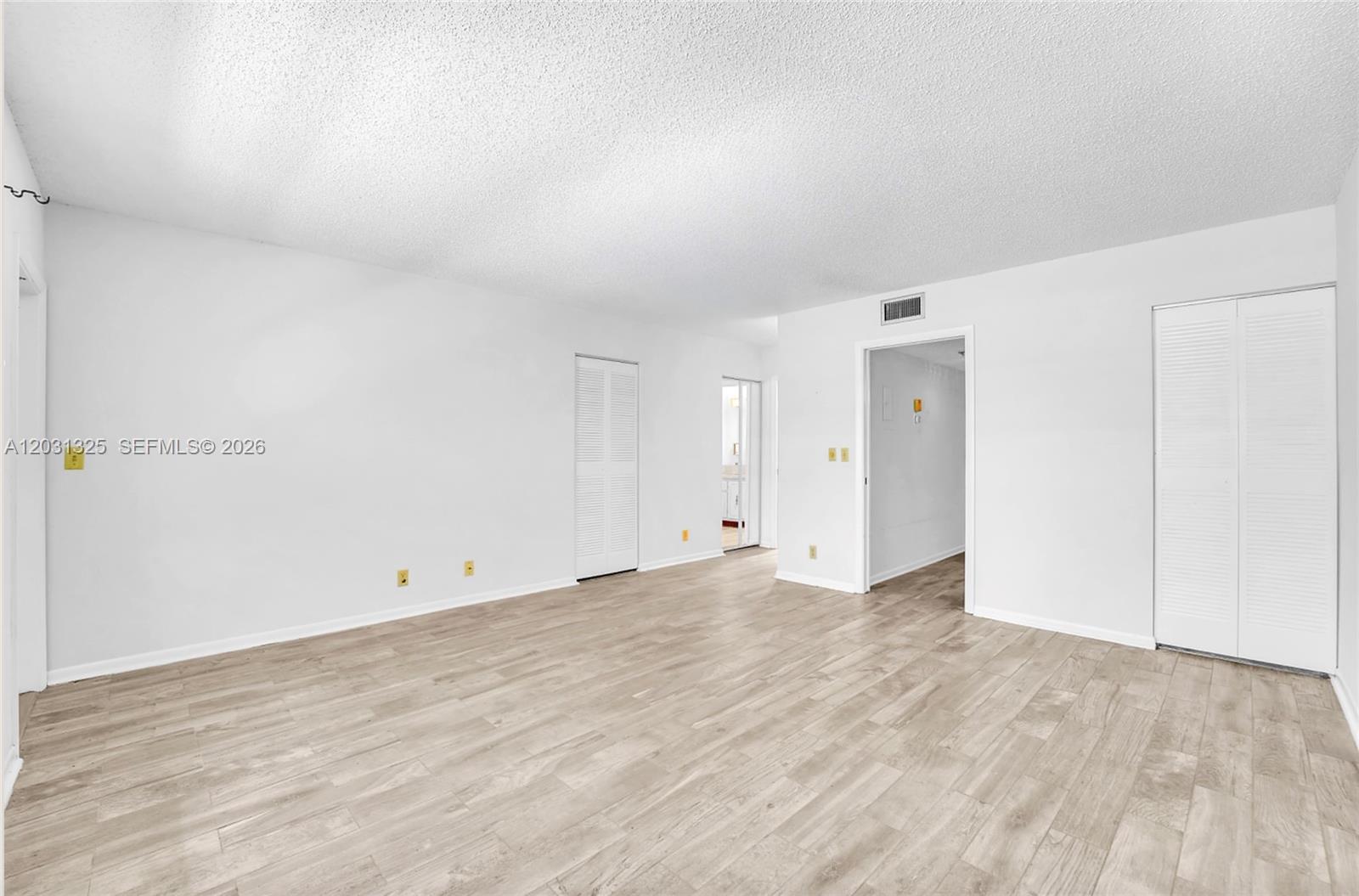 An empty room features white walls, light wood-look flooring, and two sets of louvered closet doors — 14529 Canalview Dr # B, Delray Beach FL 33484, DELRAY BEACH, FL