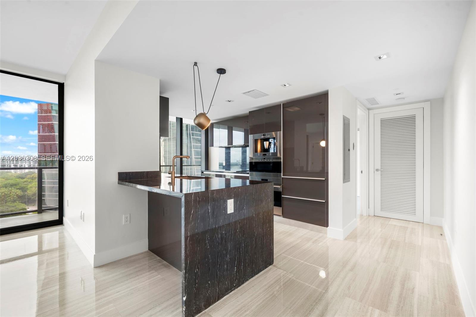 A modern kitchen features dark marble countertops, glossy brown cabinetry, and a balcony with views — 1451 Brickell Ave # 1005, Miami FL 33131, MIAMI, FL