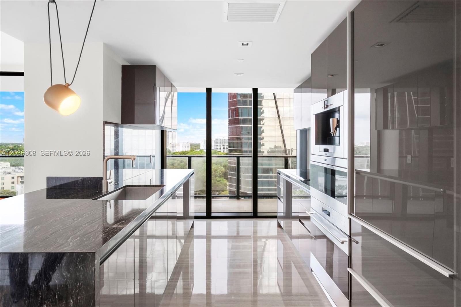 A modern kitchen features dark marble countertops, glossy cabinetry, stainless steel appliances, and floor-to-ceiling windows — 1451 Brickell Ave # 1005, Miami FL 33131, MIAMI, FL