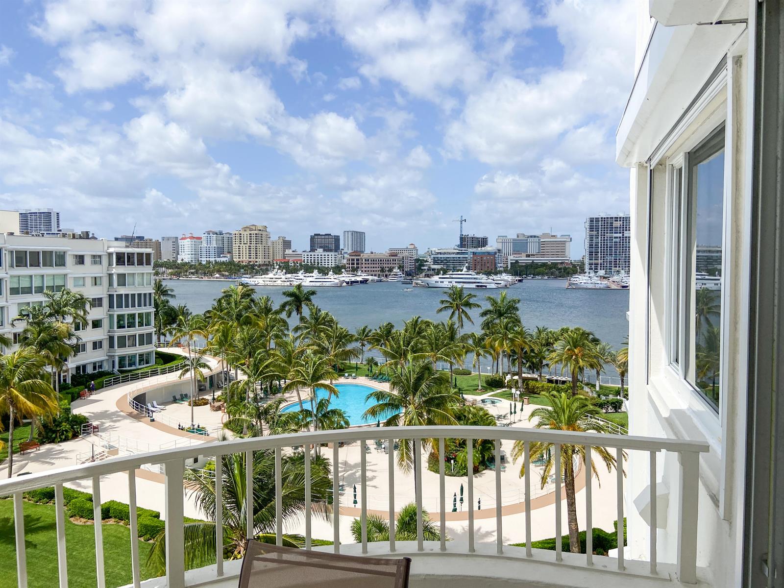 A balcony view overlooks a swimming pool, palm trees, a harbor with yachts, and city buildings — 44 Cocoanut Row # 610a, Palm Beach FL 33480, PALM BEACH, FL