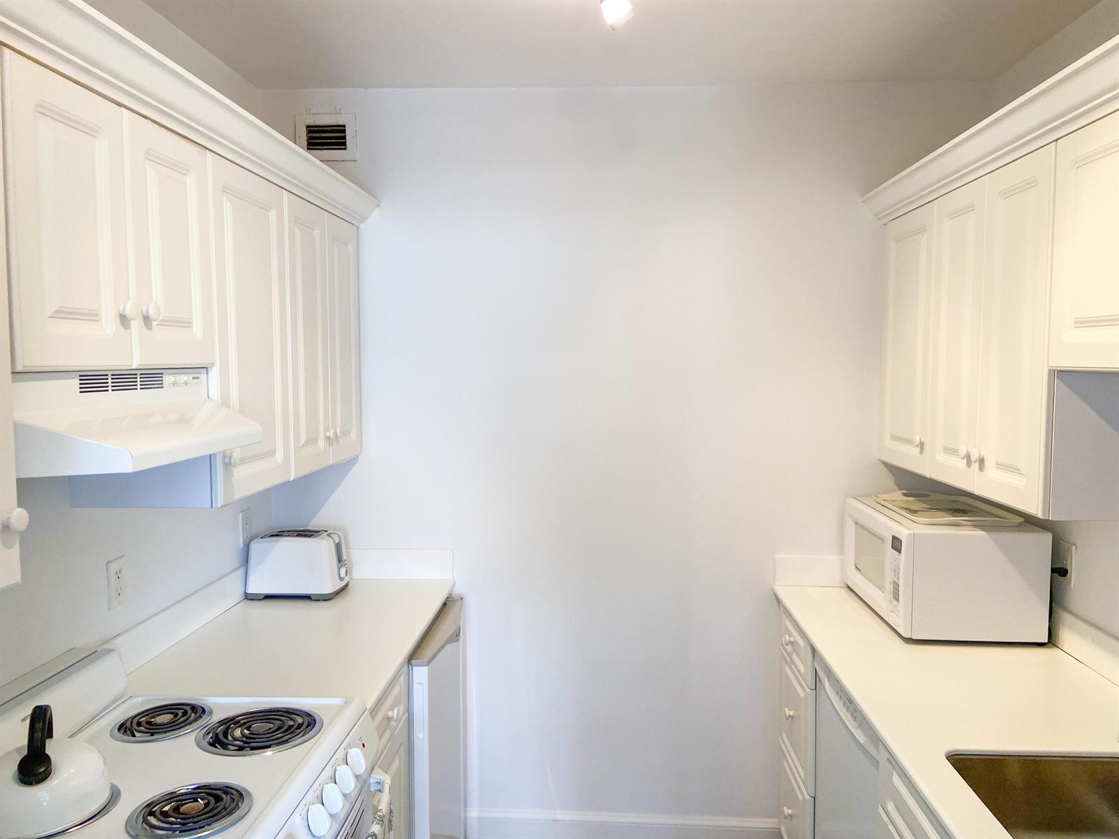A galley kitchen features white cabinets, white appliances, and white countertops on both sides — 44 Cocoanut Row # 610a, Palm Beach FL 33480, PALM BEACH, FL