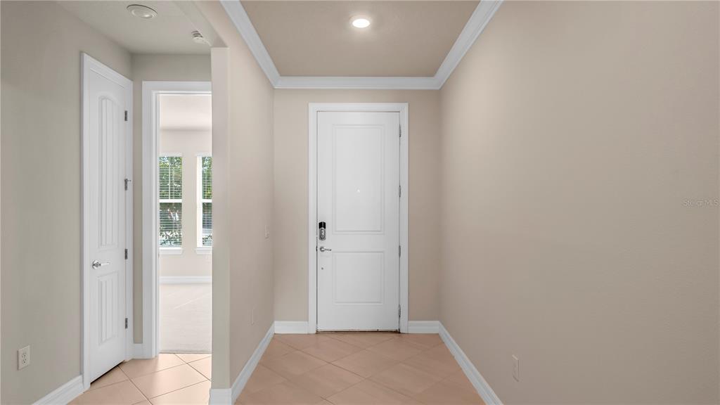 An entryway with beige walls, tile flooring, and a white front door — 9212 HANGING VINE COURT, ORLANDO, FL