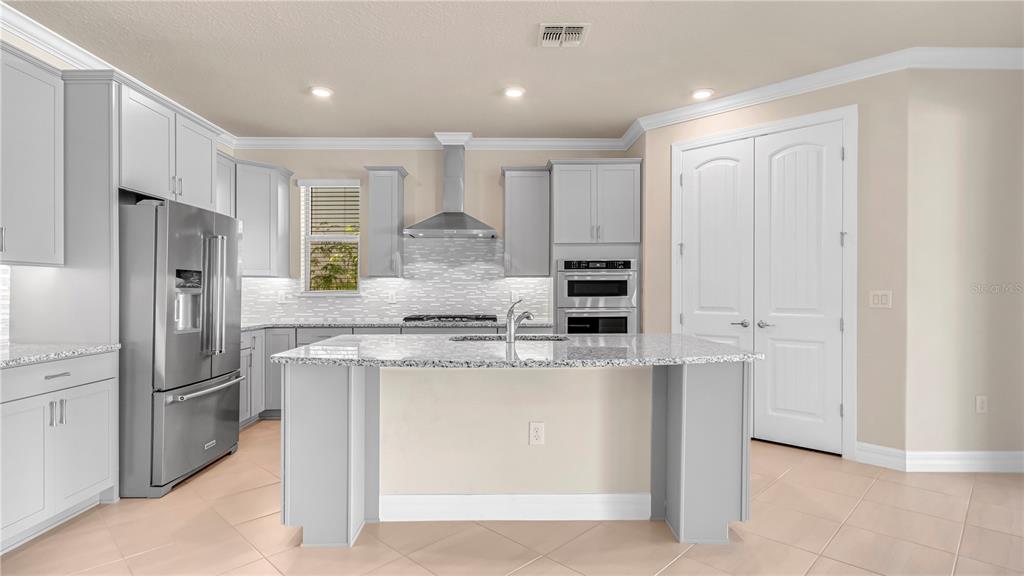 A kitchen with light gray cabinets, stainless steel appliances, a granite island, and tile flooring — 9212 HANGING VINE COURT, ORLANDO, FL