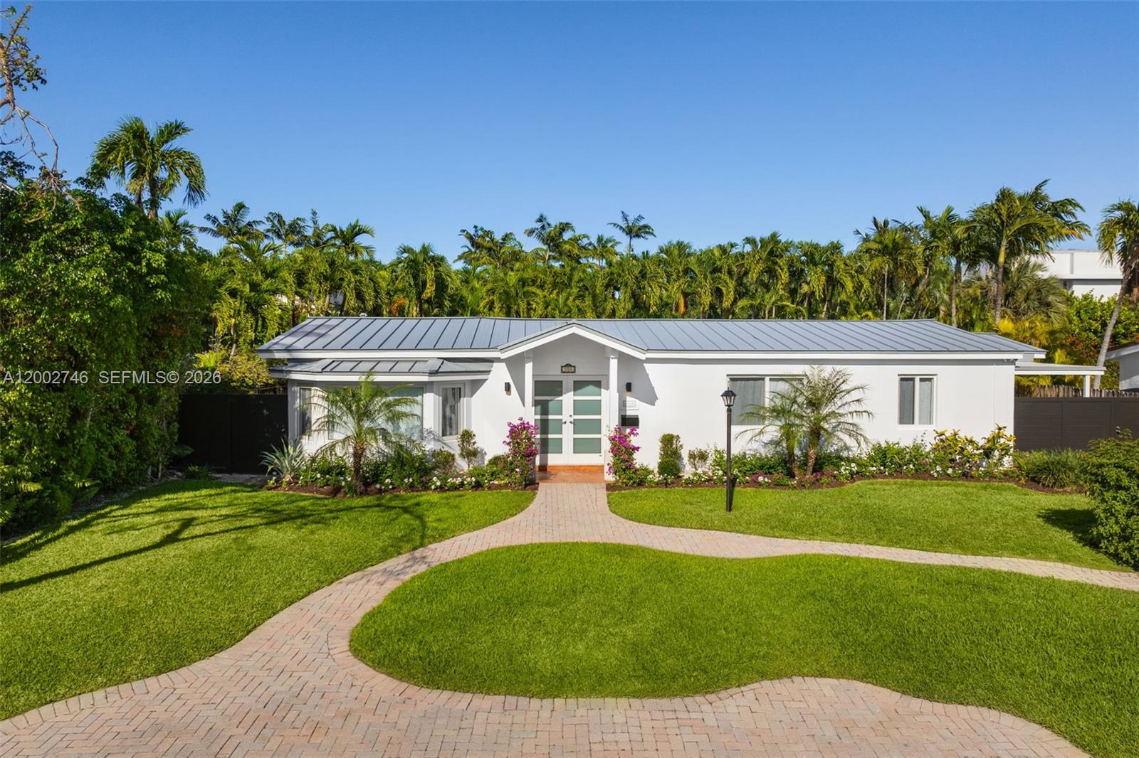 A white single-story house with a metal roof features a curved paver walkway and landscaping — 255 Ridgewood Rd, Key Biscayne FL 33149, KEY BISCAYNE, FL