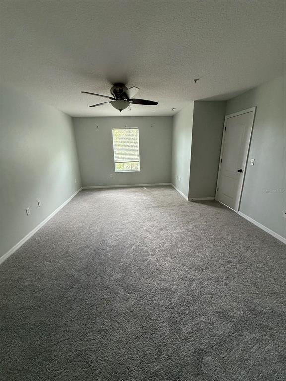 An empty bedroom features gray carpet, light gray walls, a ceiling fan, and a door — 2530 PASSAMONTE DRIVE UNIT 10E, WINTER PARK, FL