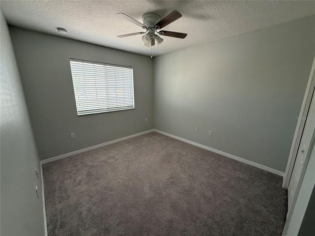 An empty bedroom features gray walls, gray carpeting, a ceiling fan, and a window with blinds — 2530 PASSAMONTE DRIVE UNIT 10E, WINTER PARK, FL