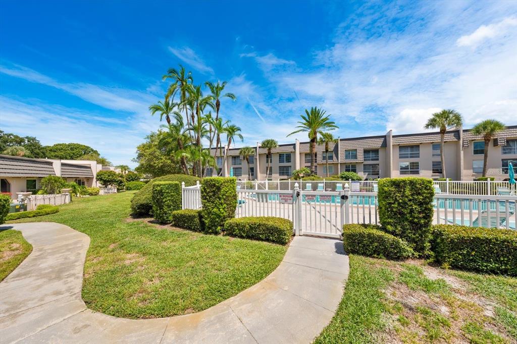 A paved walkway leads to a gated swimming pool area surrounded by landscaping and apartment buildings — 1005 CORDOVA GREEN, SEMINOLE, FL
