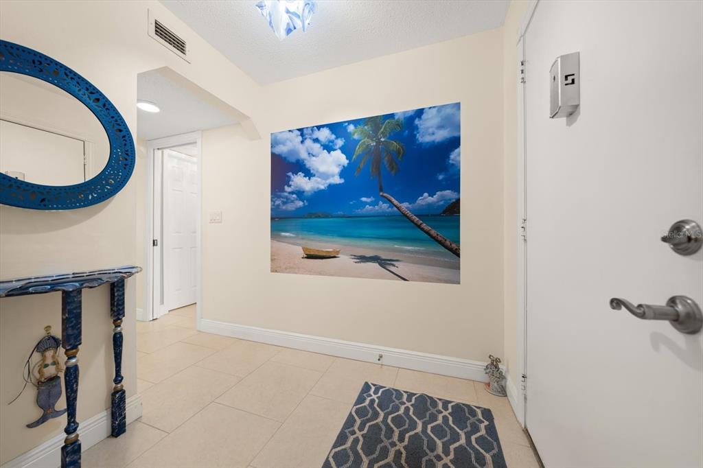 An entryway features a beach mural, a blue mirror, a console table, and tile flooring — 1005 CORDOVA GREEN, SEMINOLE, FL