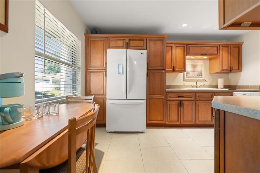 A kitchen features wood cabinets, a white refrigerator, and a dining table by a window — 1005 CORDOVA GREEN, SEMINOLE, FL