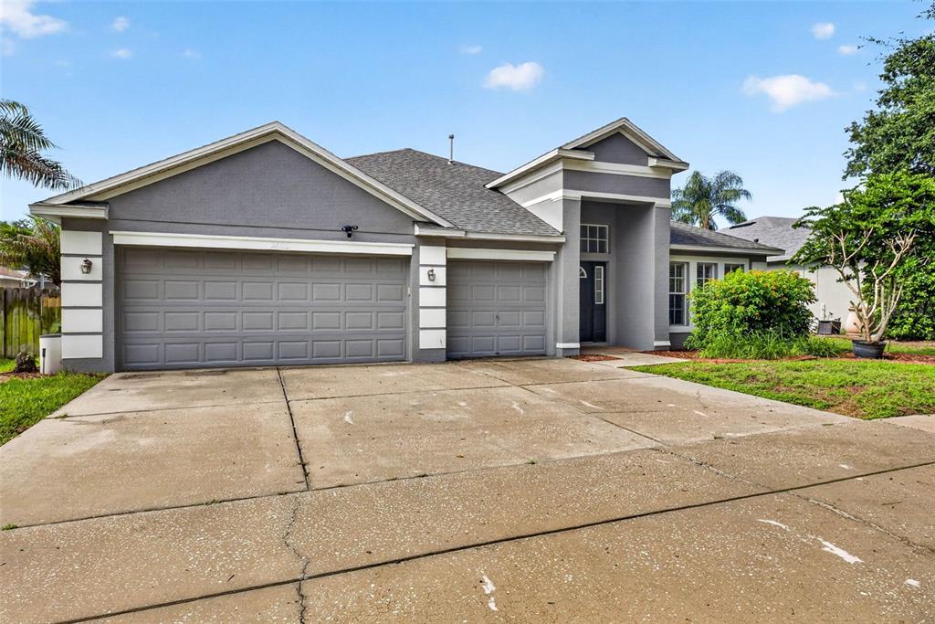 A gray single-story house features a three-car garage and a concrete driveway under a blue sky — 2605 VALENCIA GROVE DRIVE, VALRICO, FL